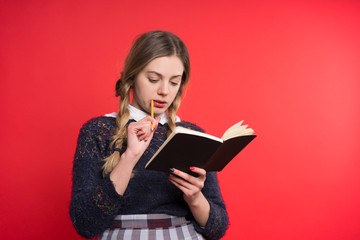 schoolgirl teen with two pigtails in a jumper and checkered skirt with a book in hand on a red background