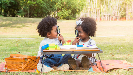 Adorable African boy and girl with afro hair looking at each other through magnifying glass with...