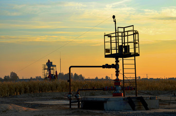 Industrial piping with steel flanges and bolts on oil field. Fuel pipes valves and crude pipelines. Gas drilling derricks at desert oilfield for fossil fuels output and crude oil production