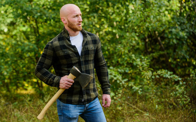 Brutal male in forest. Power and strength. Lumberjack carry ax. Bald woodsman. Harvest firewood. Hike vacation. Hike in forest. Forest care. Determination of human spirit. Man checkered shirt use axe