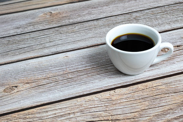 Black coffee in a white ceramic cup on a wooden table.