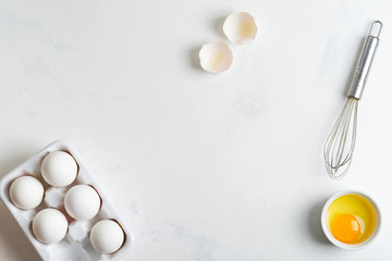 Ceramic box with natural organic farm eggs and metal whisk on a stone kitchen table.