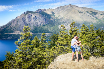 Fototapeta premium People in a mountain landscape in sunny day. Green pines and lake under the mountain in Bariloche.