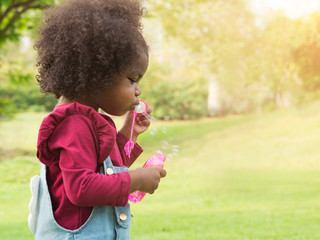 Side way, cute little girl blowing soap bubbles in the park.  Darkskinned, mixed race African child...
