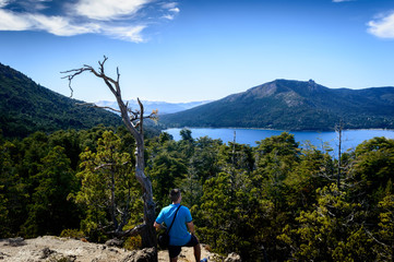 Fototapeta premium Person from back looking at the immensity of a mountain landscape with a lake at his feet. Day of sun, heat and a lot of vegetation.