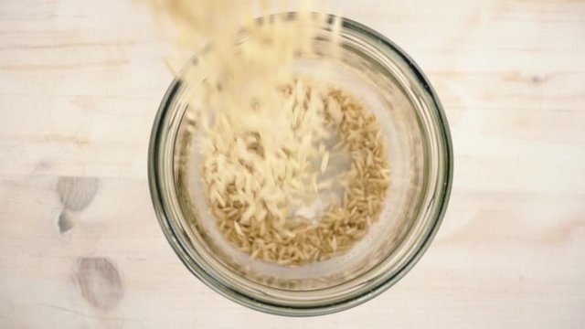 Slow motion close up top down view of brown rice grains falling in a glass jar, simple basic healthy vegan food concept theme