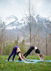 Fototapeta premium Instructor practicing yoga with female client together outdoor on grass against mountains 