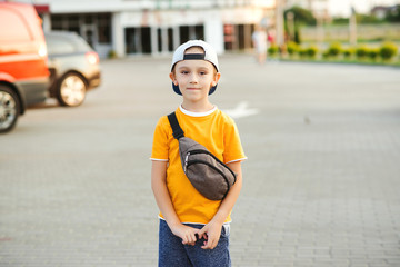 Stylish boy wearing cap outdoors. Kid with trendy banana bag at street.