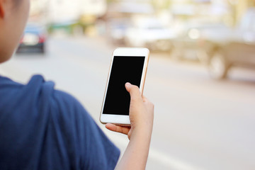 Cropped shot view of woman's hands holding smart phone with blank copy space screen for your text message or information content. Female’s hand holding phone on street side with car blur background.