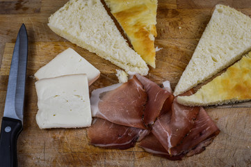 Stuffing focaccia bread with  italian smoked speck ham and taleggio cheese on a wooden cutting board close up.