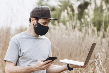 Obraz premium Freelancer during quarantine in the nature. Man in mask is working on laptop. Remote working because of corona virus. Problem of unemployment people. Covid-19 period. Self isolation.
