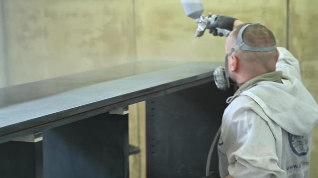 Man spraying varnish on a piece of furniture in a painting chamber