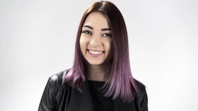 Portrait of young woman with coloured hair happily laughing at the studio. The girl in black clothes is standing at the white background and shows the emotion. Concept of different mood reflection.