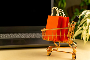 online shopping concept. little shopping cart with colorful shopping bags inside  stand near laptop