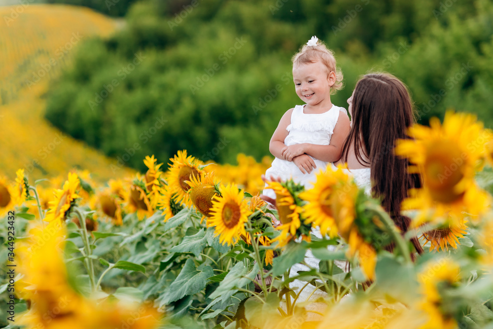 Wall mural Happy mother with the daughter in the field with sunflowers. mom and baby girl having fun outdoors. family concept.