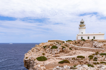 Fototapeta na wymiar Beautiful seascape with a lighthouse (Faro de Cavalleria) on a cliff and a cruise ship in the sea. Menorca, Balearic islands, Spain