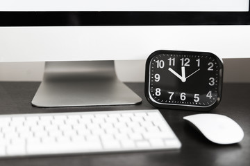 Computer with white keyboard and black clock on wooden table. Template
