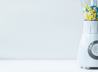 A white blender with multicolored capsules and pills. Nutritional supplementation concept. Copy space.
