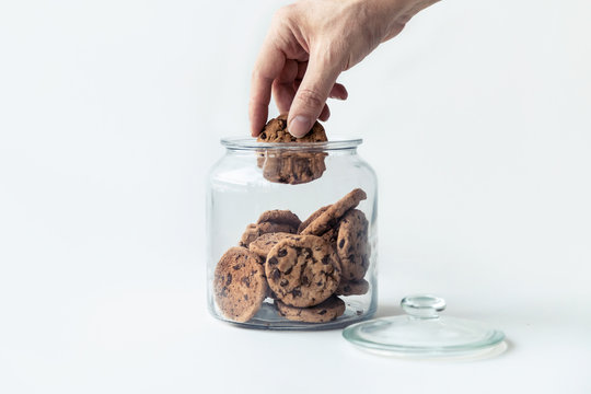 A hand taking cookies from a glass jar on white background.