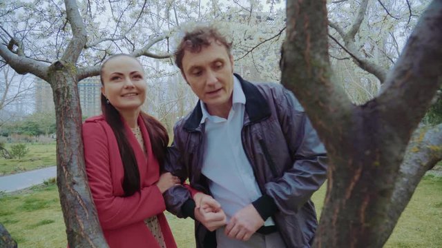A middle-aged loving couple approaches a tree in the park and talks,