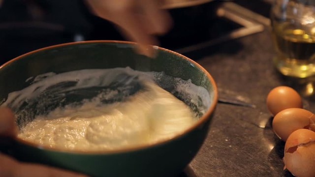 Cook mixing batter in green bowl with metal spoon egg shells and bottle of oil in background. Home cooking concept.
