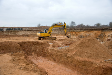 Excavator during earthworks at construction site. Backhoe digging the ground for the foundation and for laying sewer pipes district heating. Earth-moving heavy equipment