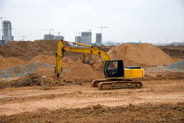 Obraz premium Excavator during earthworks at construction site. Backhoe digging the ground for the foundation and for laying sewer pipes district heating. Earth-moving heavy equipment