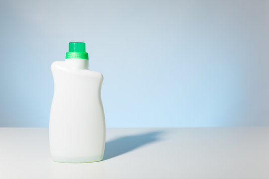 Single white detergent bottle with green cap against a pale blue bakcground.