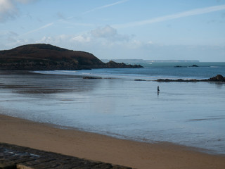 Beach at low tide in Brittany, Saint Lunaire, France. Rocks sticking out of the ocean. Mirror image in the sand. Walking man. Far on the horizon a lighthouse