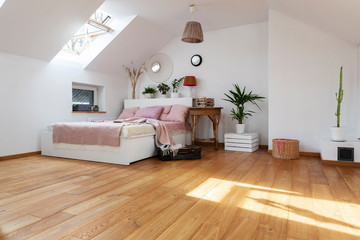 White interior of bedroom with wooden floor and double bed with pink pillows. Bright cozy bedroom in scandinavian style in the attic.