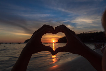 hands forming a heart shape with sunset silhouette