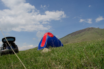 Orange tent on green grass in the mountains in summer
