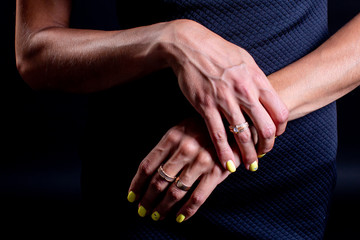 female crossed arms, dark skin, yellow false nails, gold rings on the fingers