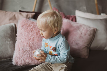 Fototapeta premium A little blond boy with a Christmas ball in his hands is studying the world around him.