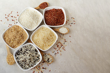 Set of different types of rice in ceramic cups on a light background: brown, red, wild rice, basmati