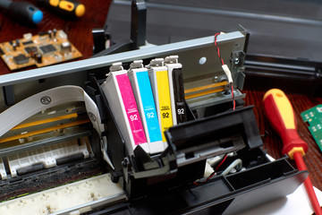 The printer is disassembled. Repair of the printer. Color ink cartridges for an inkjet printer. An inkjet printer motherboard. Maintenance of inkjet printers