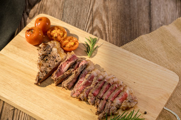 Slice Juicy grilled steak medium rare beef on wooden cutting board with tomato and rosemary , wooden table - Stock photo