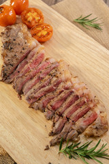 Slice Juicy grilled steak medium rare beef on wooden cutting board with tomato and rosemary , wooden table - Stock photo