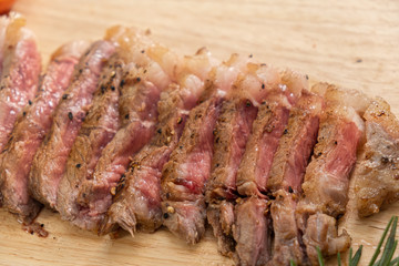 Slice Juicy grilled steak medium rare beef on wooden cutting board with tomato and rosemary , wooden table - Stock photo