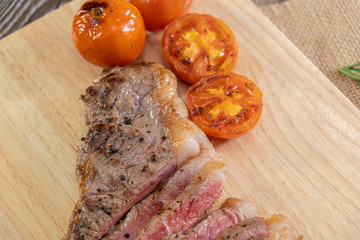 Slice Juicy grilled steak medium rare beef on wooden cutting board with tomato and rosemary , wooden table - Stock photo