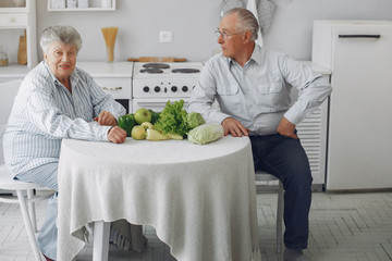 Couple in a kitchen. Grandparents sitting at home. Woman with vegetables