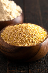 Bowls of Whole Millet and Millet Flour in Wood Bowls on a Dark Table