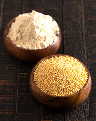 Bowls of Whole Millet and Millet Flour in Wood Bowls on a Dark Table