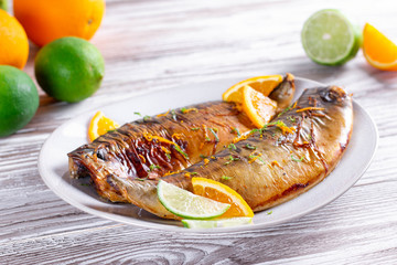 Delicious roasted fish with lime and orange slices, spices on a plate, close-up.