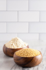 Whole Millet and Millet Flour in a Wood Bowl on a White Marble Countertop