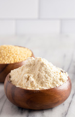 Whole Millet and Millet Flour in a Wood Bowl on a White Marble Countertop