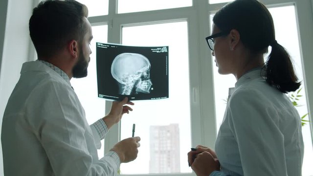 Doctors colleagues man and woman are studying x-ray image of skull working in hospital talking discussing health issues. People and medicine concept.