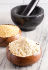 Whole Millet and Millet Flour in a Wood Bowl on a White Marble Countertop