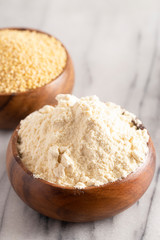 Whole Millet and Millet Flour in a Wood Bowl on a White Marble Countertop