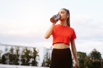 Athletic girl drinks water after a workout. Fitness woman taking a break after running.